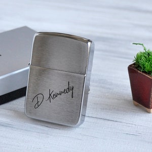 May include: A silver lighter with a brushed finish and the inscription "D. Kennedy" engraved on the front.