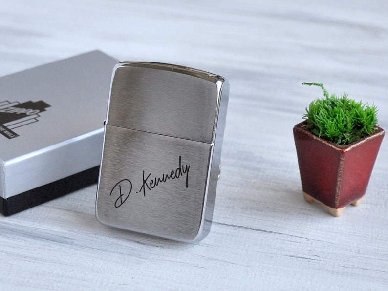 May include: A silver lighter with a brushed finish and the inscription "D. Kennedy" engraved on the front.