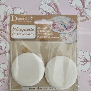 Può includere: Due placche bianche in terracotta in un sacchetto di plastica trasparente con un'etichetta marrone e bianca che dice "Decorabilia oggetti da decorare" e "Plaquette in terracotta". L'etichetta contiene anche un'immagine di un piatto in terracotta con un motivo floreale e due uccelli.