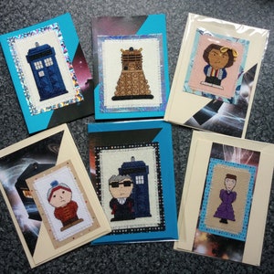 Op de afbeelding: Zes handgemaakte wenskaarten met borduurwerkontwerpen van personages en objecten uit de tv-serie Doctor Who. De kaarten zijn versierd met verschillende achtergronden, waaronder een blauwe TARDIS, een Dalek en een sterrenhemel.