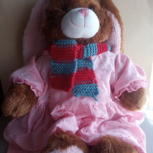 May include: A brown plush bunny wearing a pink dress and a red and blue striped scarf.