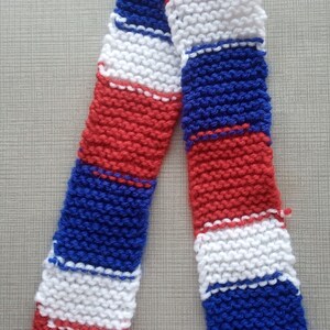 May include: A knitted scarf with red, white and blue stripes. The scarf is made from a soft, textured yarn.