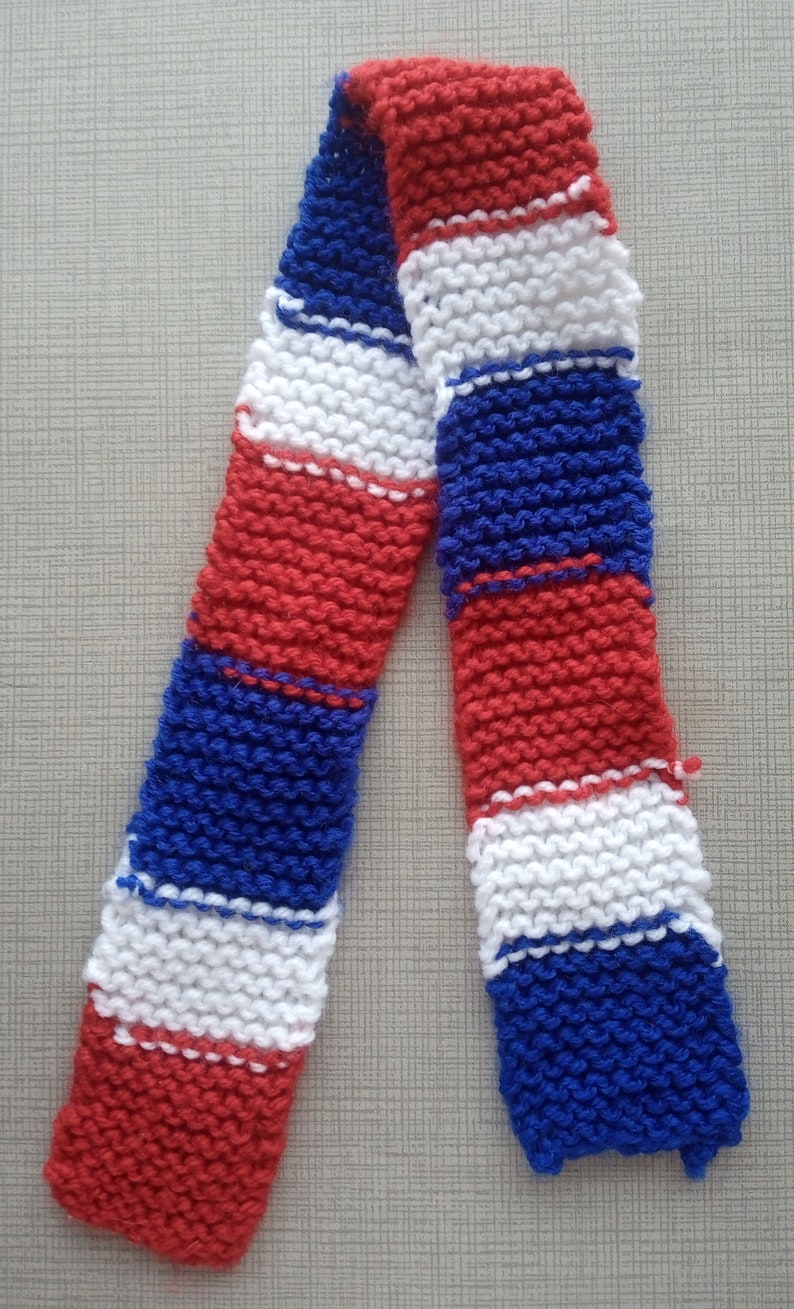 May include: A knitted scarf with red, white and blue stripes. The scarf is made from a soft, textured yarn.