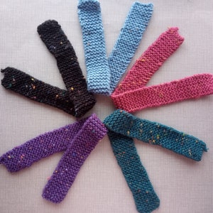 May include: Eight knitted fabric strips in various colors, including black, pink, purple, blue, and teal. The strips are arranged in a circular pattern, with the ends of each strip overlapping.