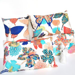 May include: Four decorative throw pillows with a white background and colorful floral and butterfly patterns. The pillows are arranged in a pyramid shape with the largest pillow at the bottom and the smallest pillow at the top.
