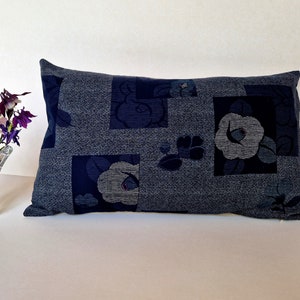 May include: A blue and grey floral patterned cushion with a geometric design. The cushion is made of a soft, textured fabric.