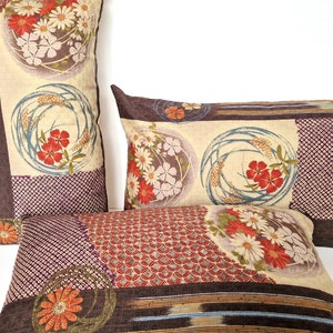 Può includere: Tre cuscini decorativi con un motivo floreale di ispirazione giapponese. I cuscini sono realizzati in tessuto marrone con uno sfondo beige e presentano una varietà di motivi floreali in tonalità di rosso, arancione, bianco e blu.