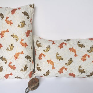 May include: Two decorative throw pillows with a white background and a pattern of orange and brown fish swimming in a wavy pattern.