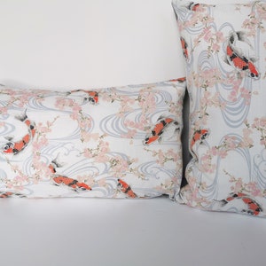 May include: Two decorative pillows with a Japanese-inspired design. The pillows feature a white background with a pattern of koi fish, cherry blossoms, and flowing water in shades of red, pink, and gray. One pillow is rectangular, the other is square.