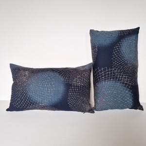 May include: Two decorative throw pillows featuring a geometric pattern in shades of blue and white. The pattern resembles a net or mesh with a subtle pink accent.