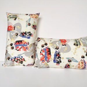 Peut inclure: Deux coussins décoratifs avec un fond blanc et un motif de femmes en vêtements traditionnels japonais avec des éventails et des parapluies. Le motif est dans des tons de rouge, bleu, noir et or.