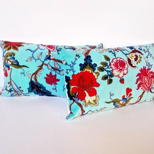 May include: Two turquoise blue velvet pillow covers with a floral pattern in shades of red, pink, and green. The floral pattern features large flowers and leaves.