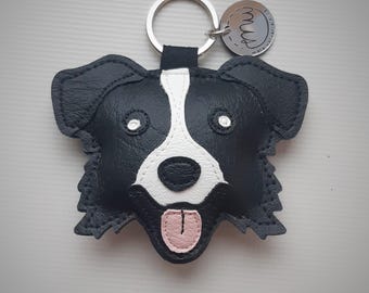 May include: Black and white leather border collie dog keychain with a pink tongue and a silver keyring with a small silver tag that says "Mugs".