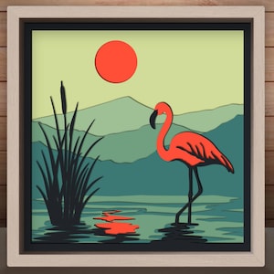 May include: A layered art piece featuring a flamingo in a serene landscape. The artwork showcases a vibrant orange flamingo standing in water, with a red sun in the sky and green mountains in the background. The piece is framed in a light-colored wooden frame.