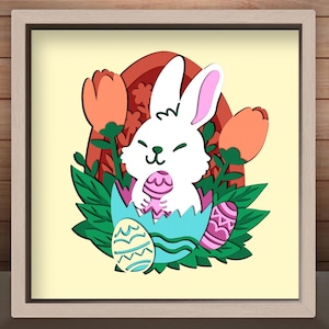 May include: A framed Easter-themed artwork featuring a white bunny holding a pink egg, emerging from a cracked blue eggshell. The design includes orange tulips, green leaves, and decorative Easter eggs. The artwork is set against a light yellow background.