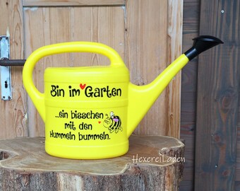 May include: Yellow watering can with a black handle and spout. The can has a red heart and the text "Bin im Garten...ein bisschen mit den Hummeln bummeln." printed on it.