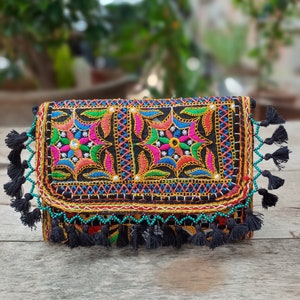 May include: Black clutch with colorful embroidered floral patterns. The clutch features a flap closure, black tassels, and turquoise bead accents. The embroidery includes pink, blue, green, and yellow thread.