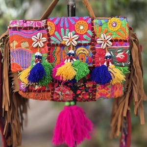 Puede incluir: Bolso de hombro patchwork colorido con asa y correa marrones. El bolso presenta diseños florales bordados, conchas marinas y borlas de cuentas en varios colores. El bolso tiene flecos en los laterales y una borla rosa grande.
