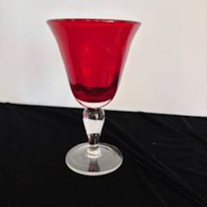 May include: A red glass wine goblet with a clear glass stem and base.