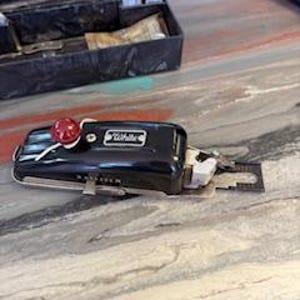 May include: A black sewing machine with a red button and a silver needle. The machine is small and compact, and it is designed for sewing fabric.