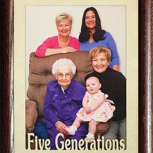 May include: A framed photo of five generations of a family. The photo shows a grandmother, great-grandmother, mother, daughter, and granddaughter. The photo is in a brown frame with a cream mat. The text "Five Generations" is printed below the photo.