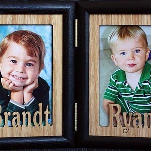 May include: Two wooden picture frames with black borders. Each frame has a photo of a young boy. The frame on the left has the name "Brandt" cut out of the wood below the photo. The frame on the right has the name "Ryan" cut out of the wood below the photo.
