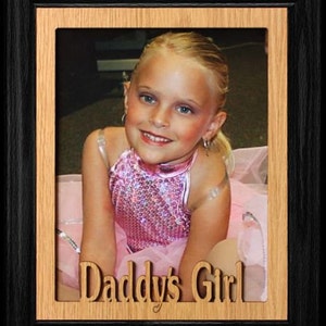 May include: A framed photo of a young girl wearing a pink sequined dress and a white tutu. The frame is made of wood and has the words "Daddy's Girl" carved into it.