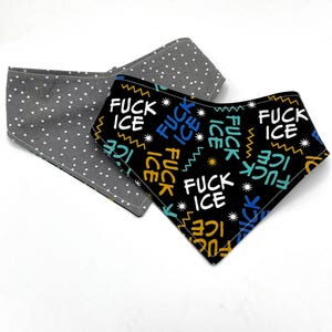 May include: Two dog bandanas. One is gray with white polka dots. The other is black with the words "FUCK ICE" in white, yellow, blue, and teal. The bandanas are made of fabric and are triangular in shape.