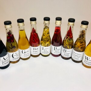 May include: Ten glass bottles of infused vinegar with various flavors, including aged balsamic, cranberry sage, garlic lovers, hot pepper, lemon & thyme, purple basil, rosemary & hot pepper, rosemary & lemon, and white balsamic.