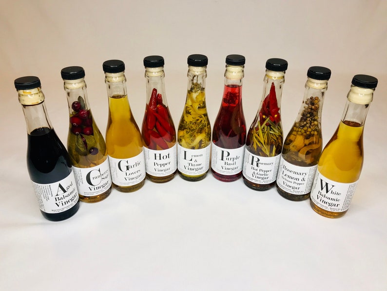 May include: Ten glass bottles of infused vinegar with various flavors, including aged balsamic, cranberry sage, garlic lovers, hot pepper, lemon & thyme, purple basil, rosemary & hot pepper, rosemary & lemon, and white balsamic.
