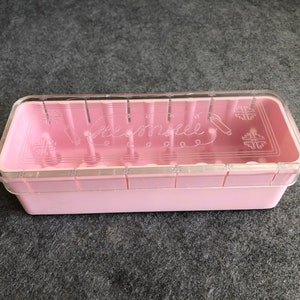 May include: A pink plastic storage box with a clear lid. The lid has the word "Homespun" printed on it.