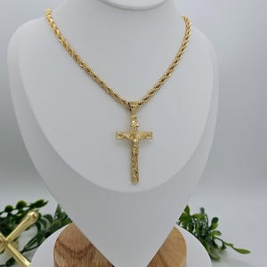 May include: A gold-tone rope chain necklace with a detailed gold-tone crucifix pendant.