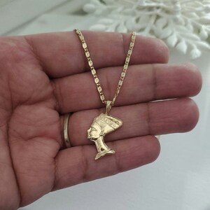 May include: A gold chain necklace with a pendant featuring a profile of an Egyptian queen wearing a headdress.