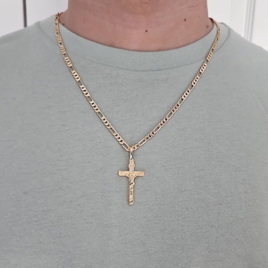 Puede incluir: Un collar de cadena de oro con un colgante de cruz de oro. La cadena es de estilo figaro.