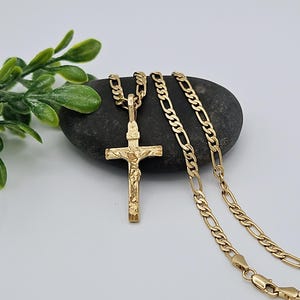 May include: A gold chain necklace with a detailed gold crucifix pendant. The chain is a classic figaro style.