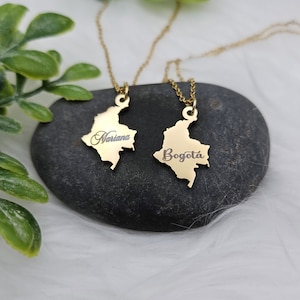 May include: Two gold necklaces with pendants shaped like the outline of Colombia. One pendant says "Mariana" and the other says "Bogota".