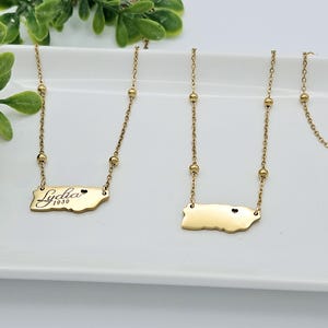 May include: Two gold necklaces with a small heart charm and a pendant shaped like the island of Puerto Rico. One pendant has the name "Lydia 1959" engraved on it.