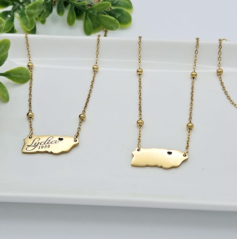 May include: Two gold necklaces with a small heart charm and a pendant shaped like the island of Puerto Rico. One pendant has the name "Lydia 1959" engraved on it.