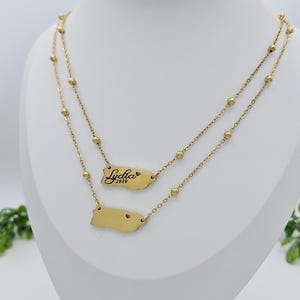May include: Gold layered necklace with a small charm of the outline of Puerto Rico and a larger charm with the name "Lydia" and the year "1989" engraved on it.