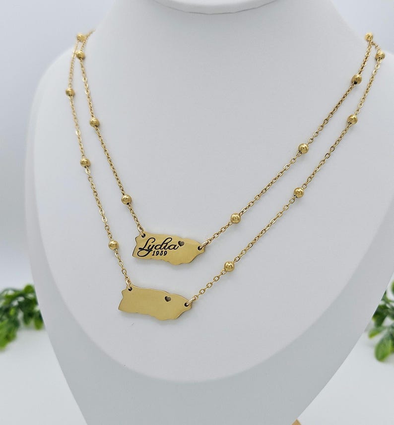 May include: Gold layered necklace with a small charm of the outline of Puerto Rico and a larger charm with the name "Lydia" and the year "1989" engraved on it.