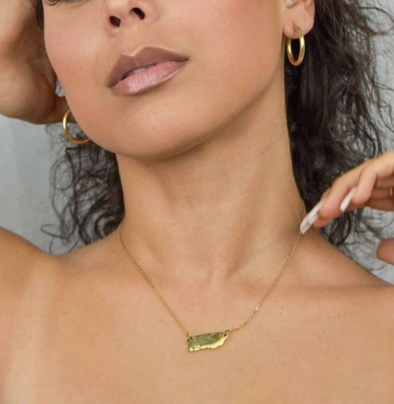 May include: A gold chain necklace with a pendant shaped like the island of Puerto Rico.