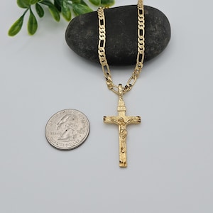 Puede incluir: Un collar de cadena de oro con un colgante de crucifijo de oro. El colgante presenta una representaci&oacute;n detallada de Jesucristo en la cruz. La cadena es de estilo figaro cl&aacute;sico.