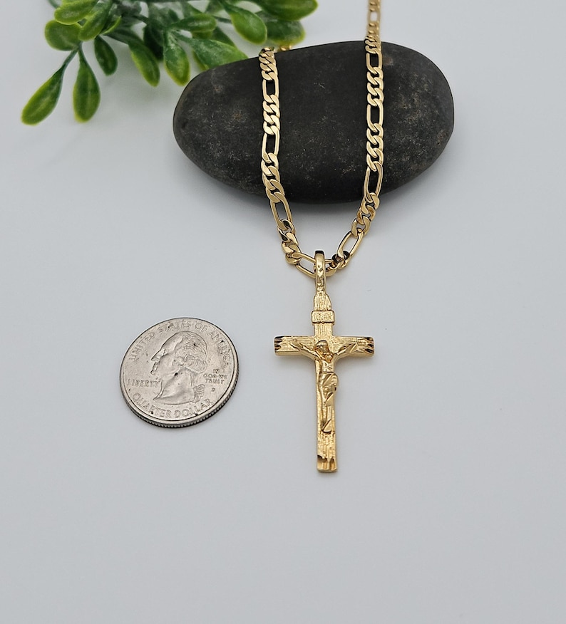 Puede incluir: Un collar de cadena de oro con un colgante de crucifijo de oro. El colgante presenta una representaci&oacute;n detallada de Jesucristo en la cruz. La cadena es de estilo figaro cl&aacute;sico.