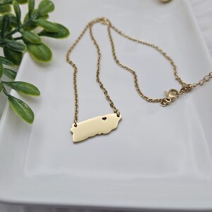 May include: A gold chain necklace with a pendant shaped like the island of Puerto Rico. The pendant has a small heart cut out in the center.