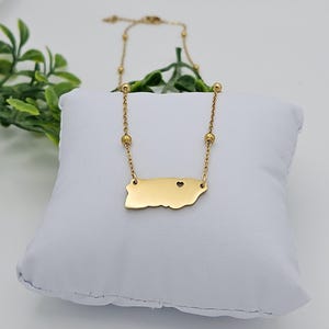 May include: Gold necklace with a pendant shaped like the outline of Puerto Rico with a small heart cut out in the center.