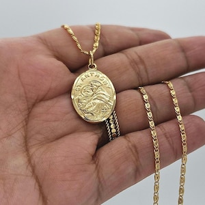 May include: Gold-colored pendant necklace featuring an oval medallion with an embossed image of St. Anthony and the text "ST. ANTHONY". The necklace has a delicate chain.
