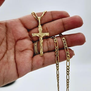 Puede incluir: Un collar de cadena de oro con un colgante de oro de Jes&uacute;s en la cruz. La cadena es de estilo Cuban link y el colgante est&aacute; detallado con un acabado texturizado.