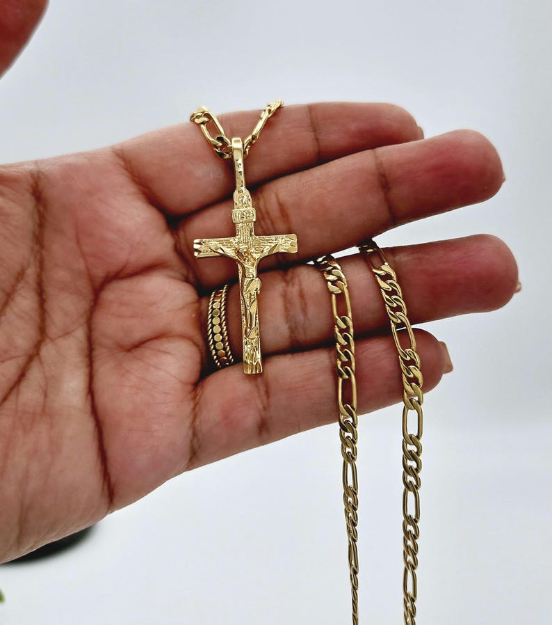 Puede incluir: Un collar de cadena de oro con un colgante de oro de Jes&uacute;s en la cruz. La cadena es de estilo Cuban link y el colgante est&aacute; detallado con un acabado texturizado.