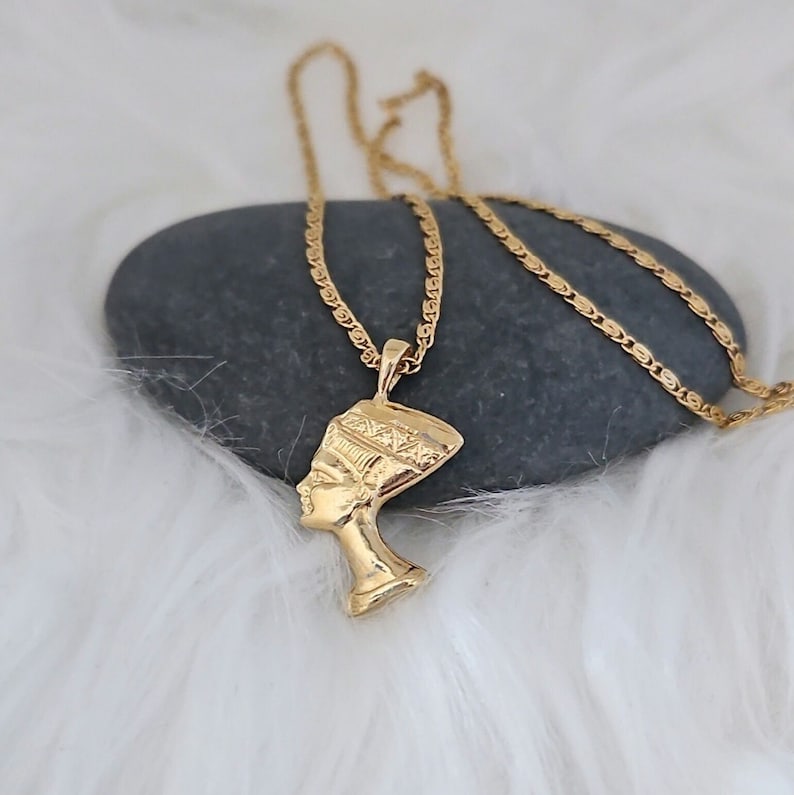 May include: Gold chain necklace with a pendant featuring a profile of an Egyptian queen wearing a headdress.