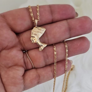 May include: Gold chain necklace with a pendant featuring a profile of an Egyptian queen wearing a headdress.